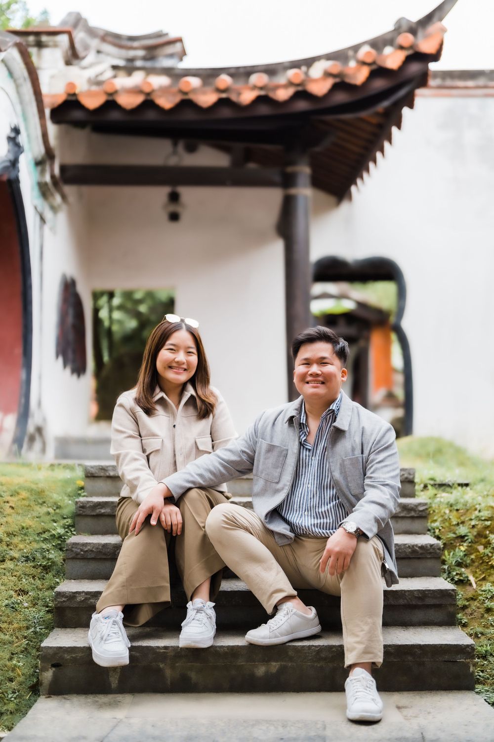 Couple sitting on stone steps in front of traditional Asian architecture with tiled roof.