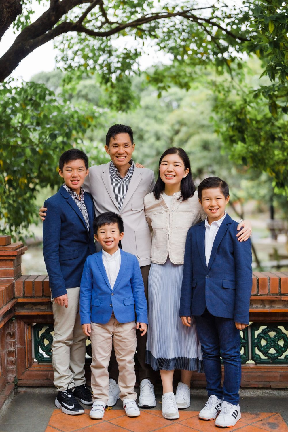 Family of five dressed in coordinating blue and beige outfits pose together in front of lush greenery.