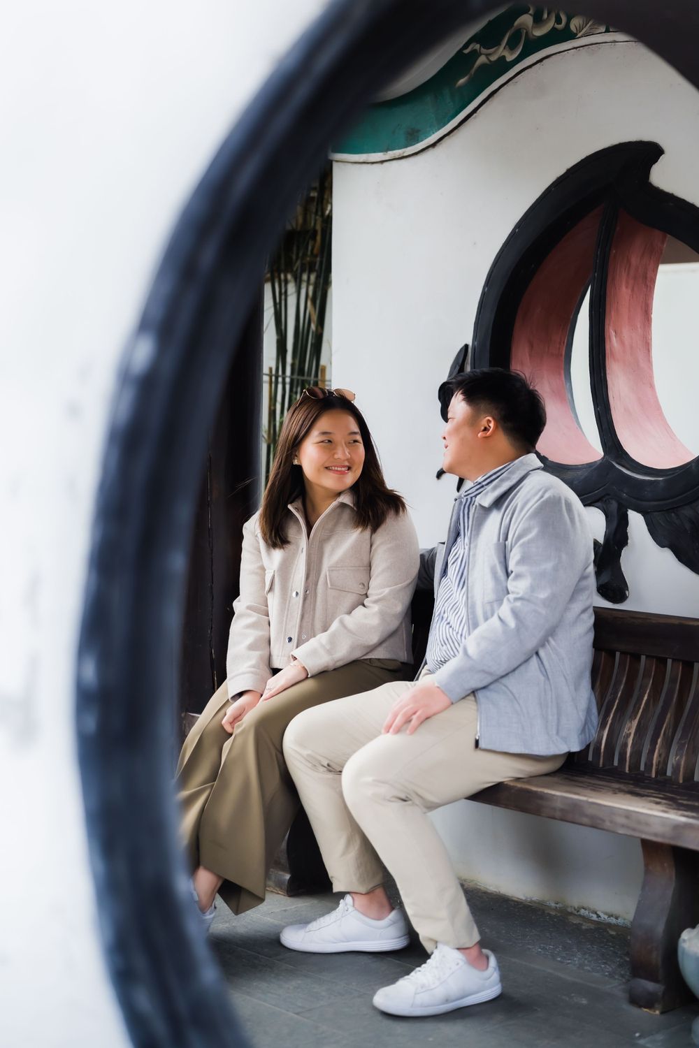 Couple sharing happy moment on bench viewed through circular architectural frame.
