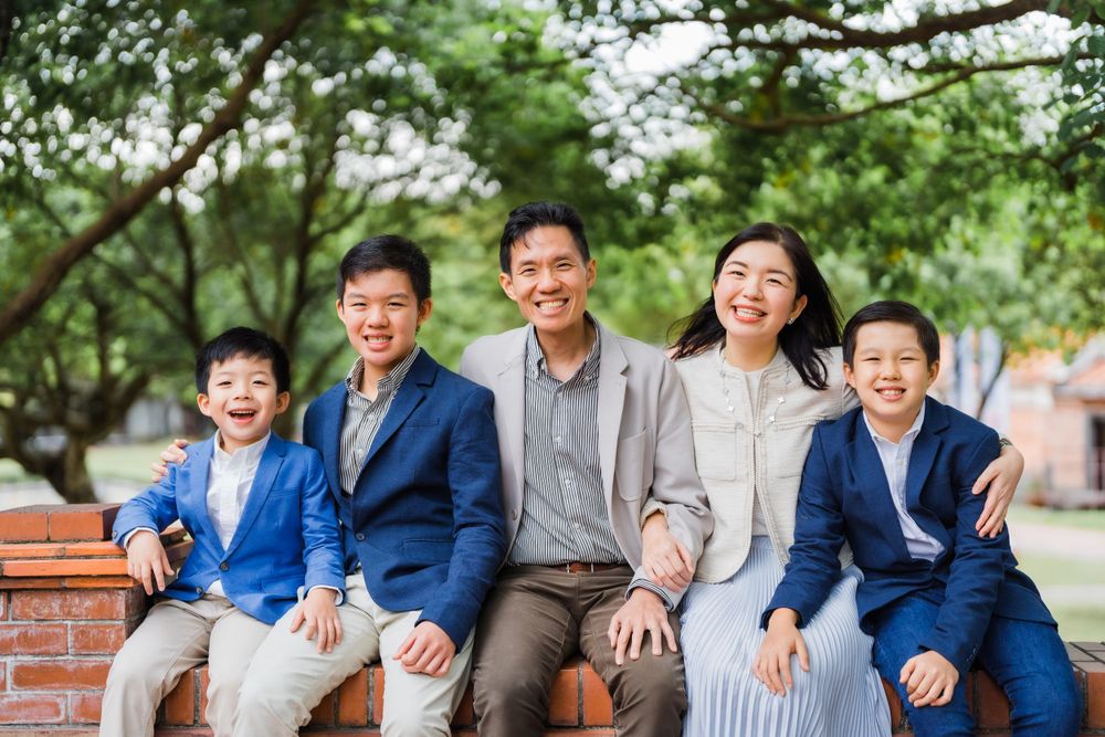 Family in coordinated blue and neutral outfits smiling together on brick wall outdoors.