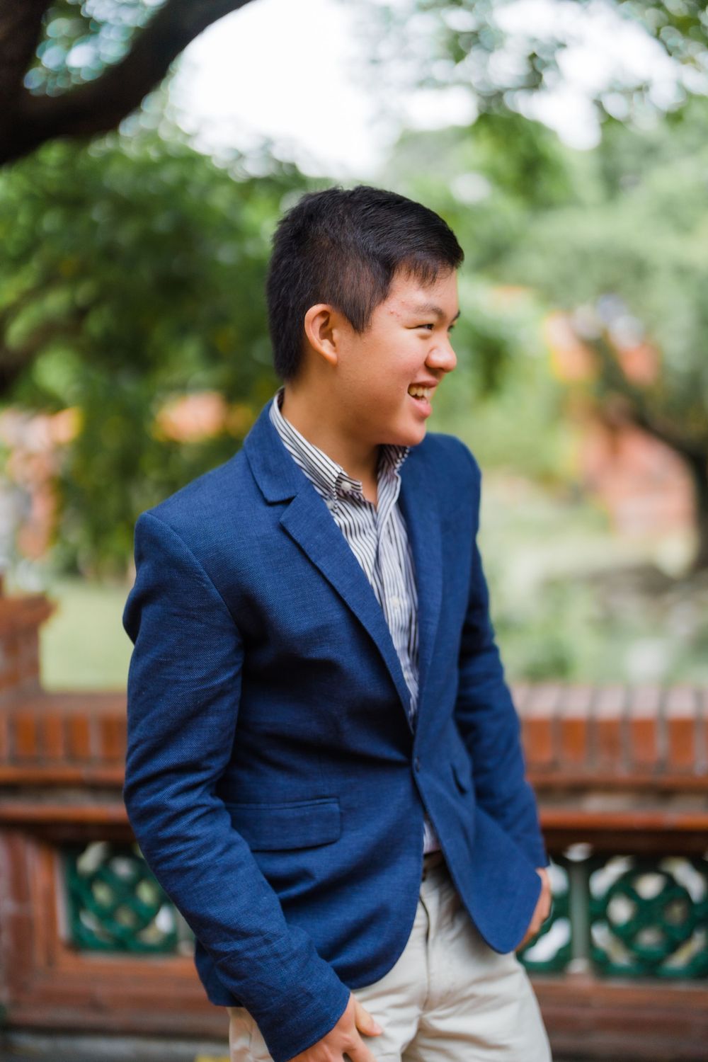 Young person in navy blazer smiling while standing against blurred green background.