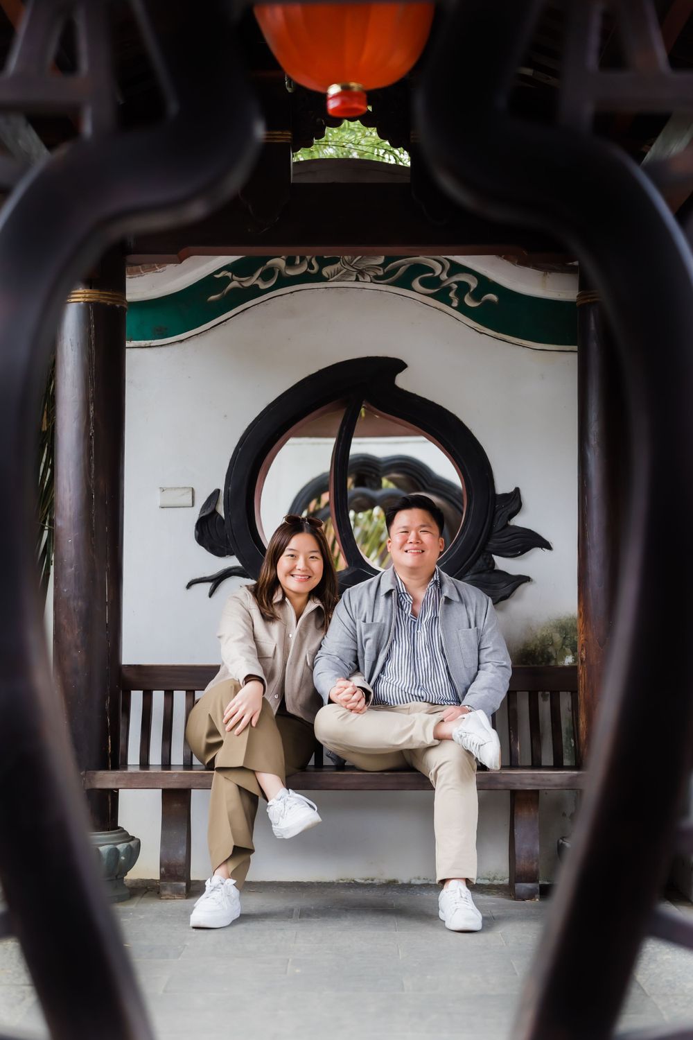 Couple sitting together on bench framed by decorative circular window and orange lantern.