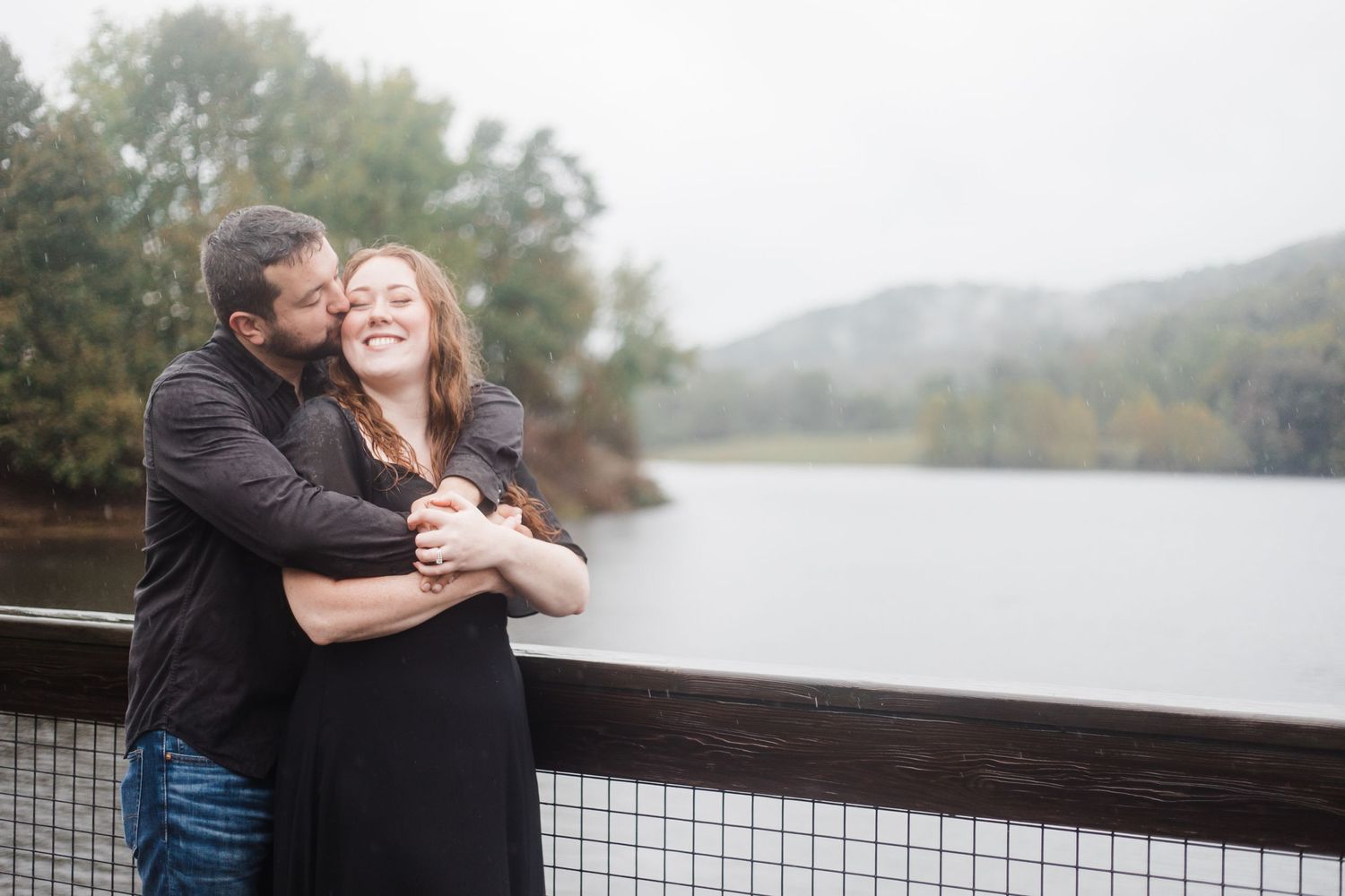 Romantic couple embraces on wooden boardwalk overlooking misty lake during autumn day.