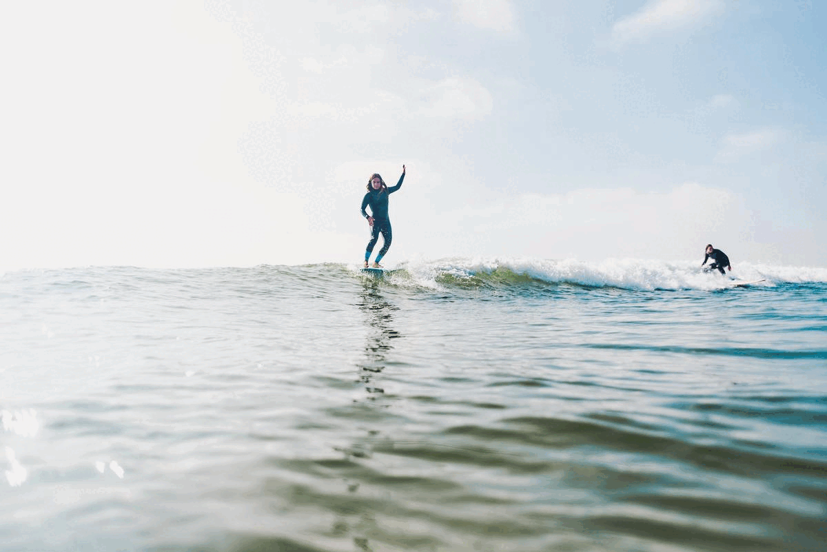 Surfers ride ocean waves on a bright sunny day with clear blue skies.