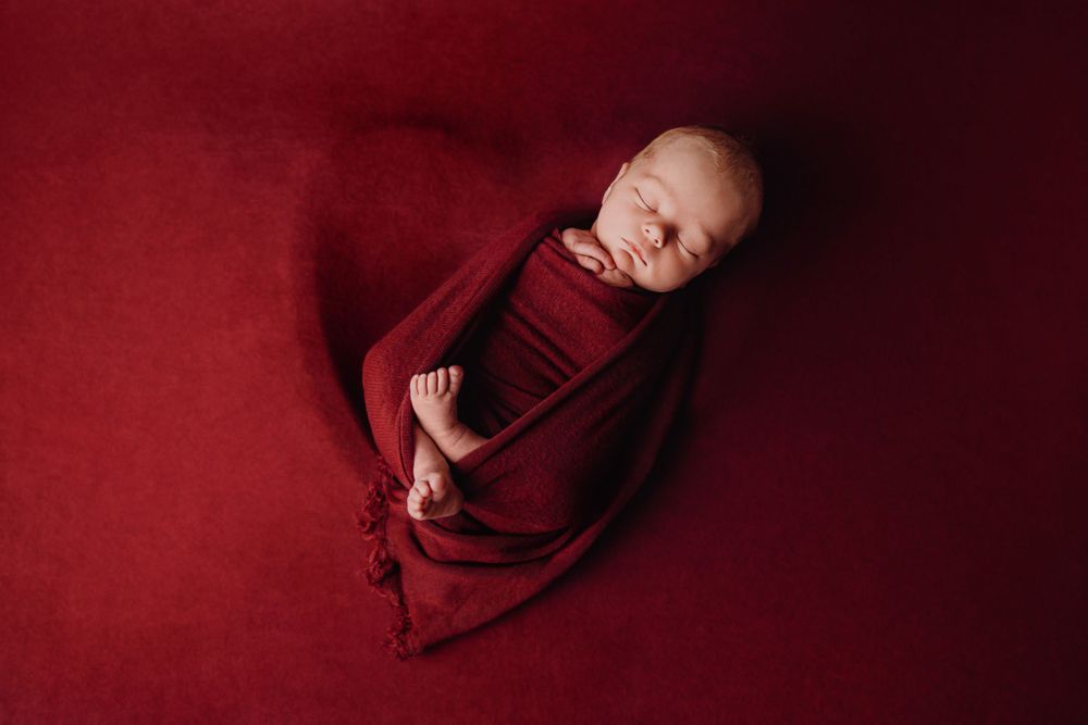 Friedliches Neugeborenes Baby in tiefroten Stoff auf passendem rotem Hintergrund.