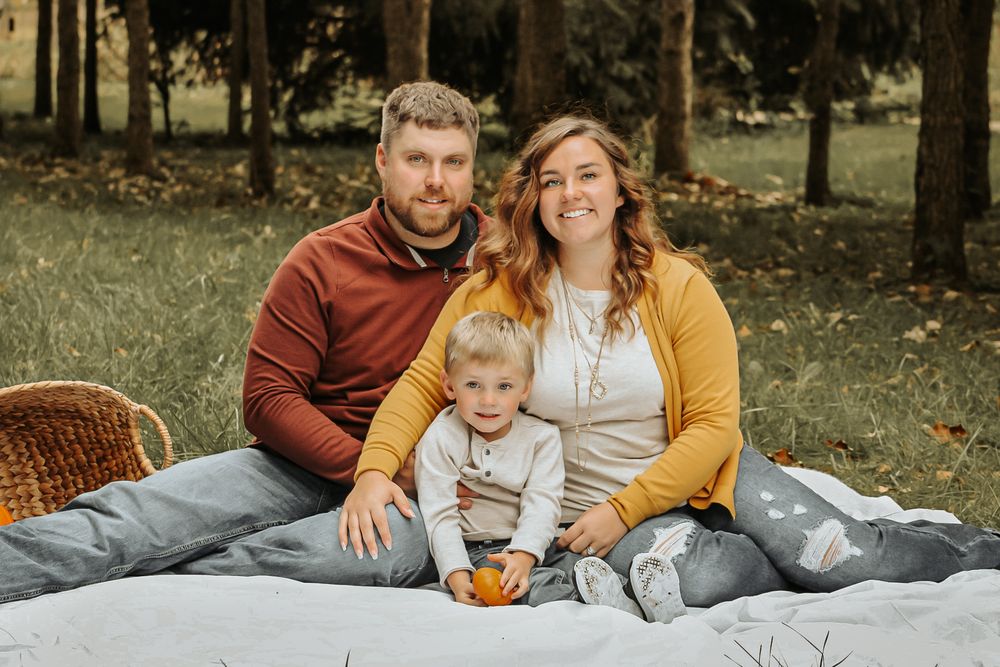 Family relaxes together on a blanket during an outdoor autumn photoshoot in a park setting.