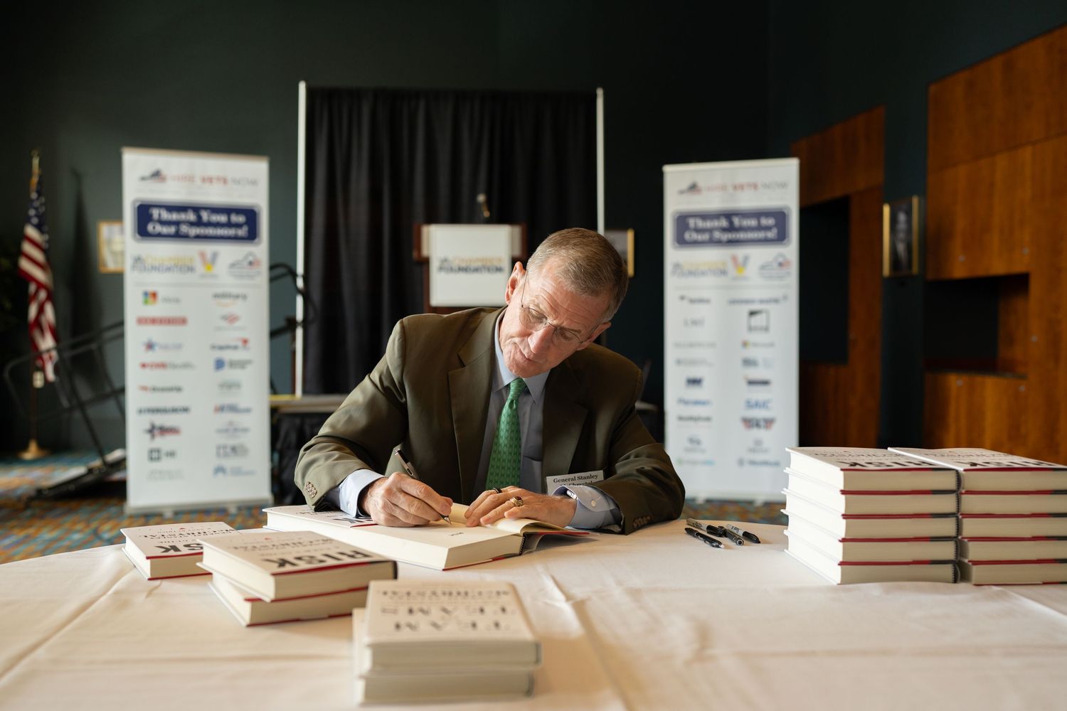Author signs books at a professional event with sponsor banners in background, highlighting thought leadership and business engagement.