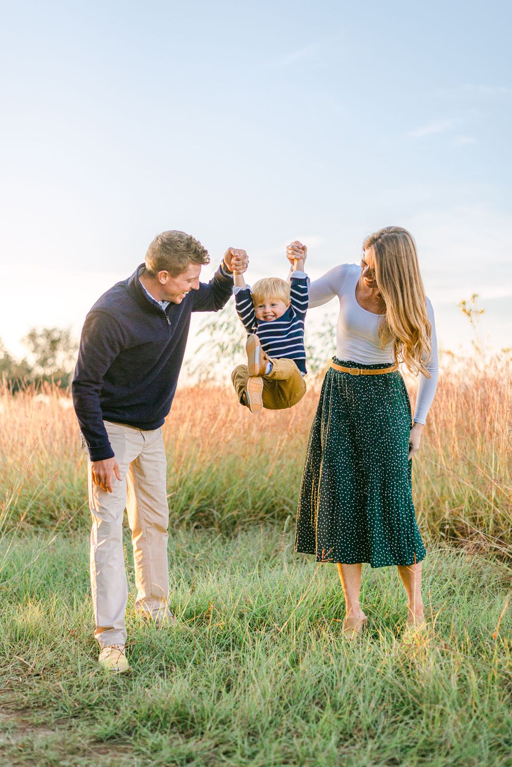 a mom and dad swing their two year old boy between them laughing