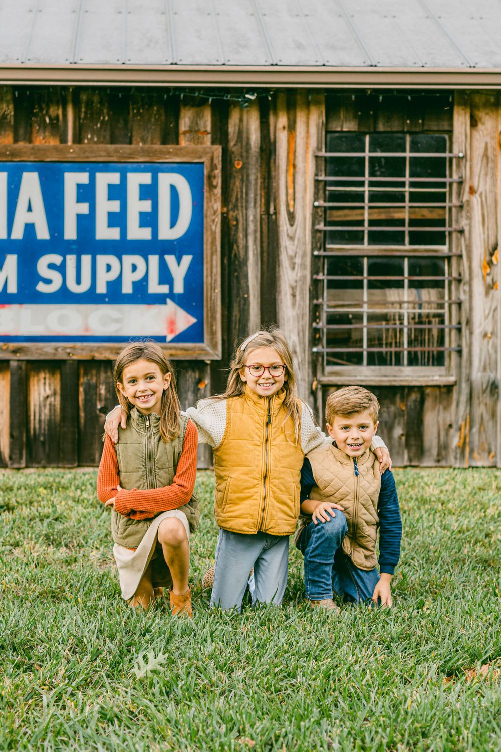 three kids with their arms around each other smiling in front of an old wooden building