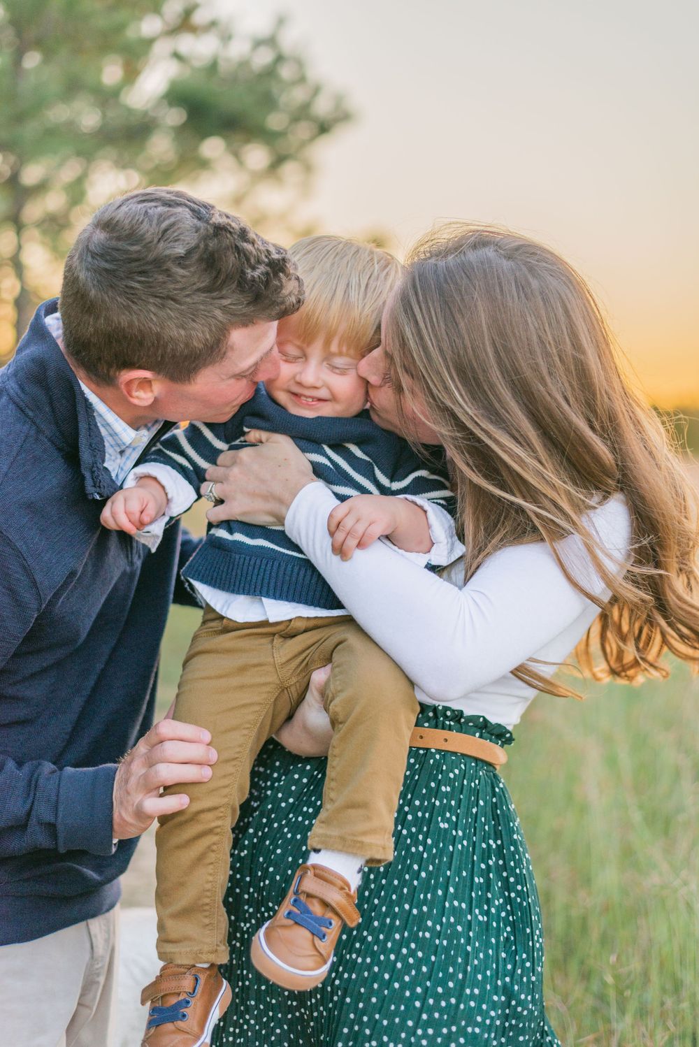 a mom and dad sandwich their little boy with kisses