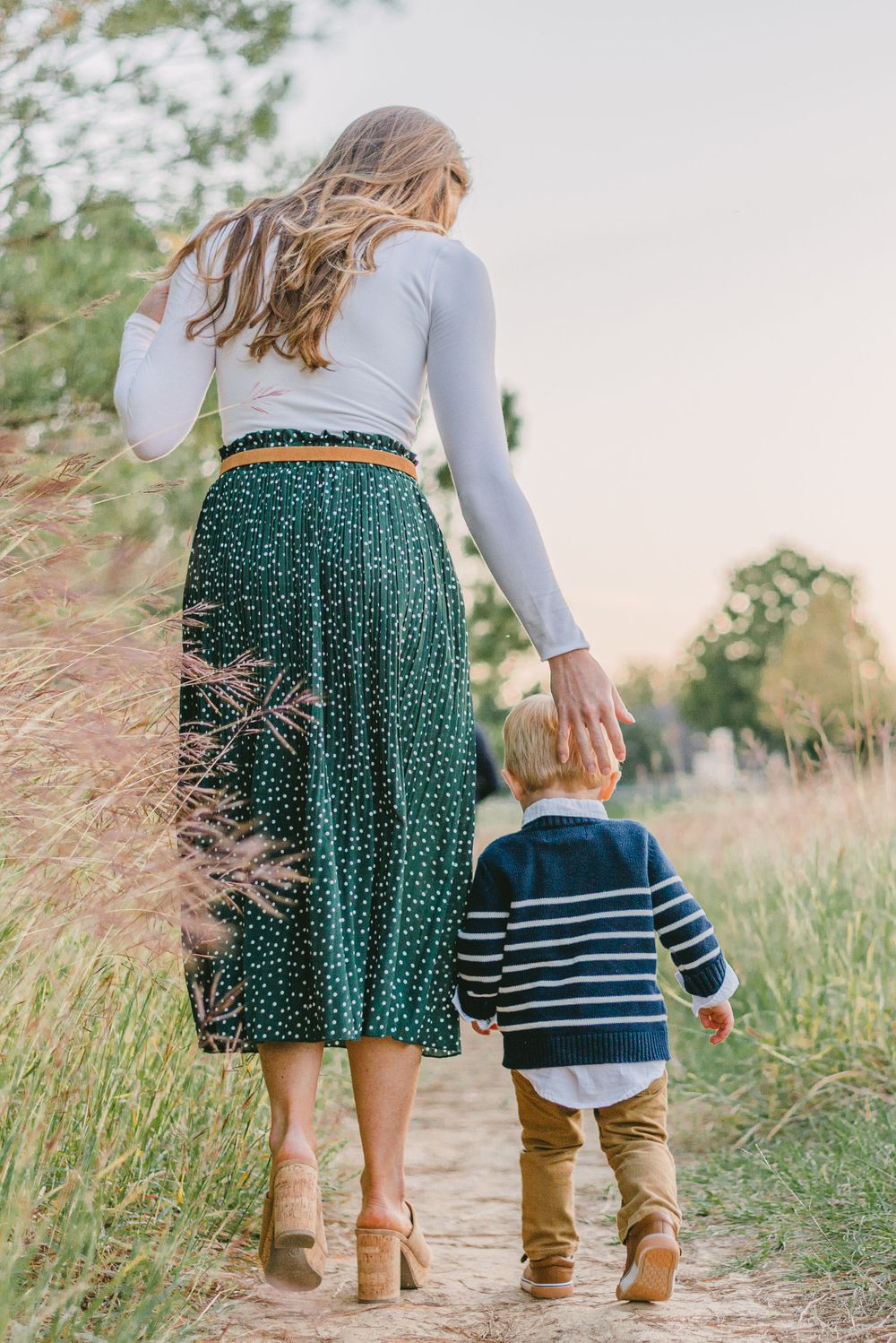 a woman gently guides her son along a trail among the tall grass