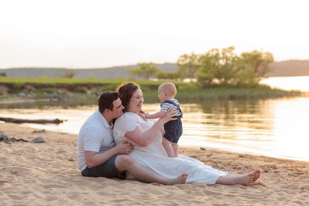 A mom and dad sit on the beach just before sunset with their baby boy in mom's lap.