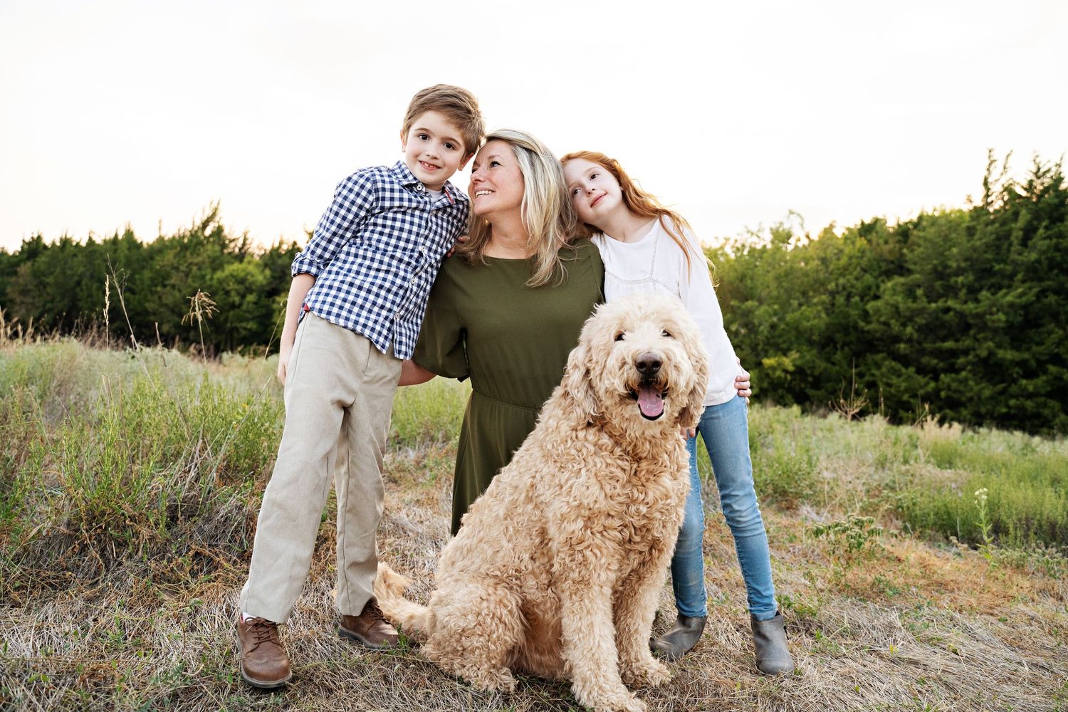 Family and goldendoodle dog posing together outdoors at sunset.