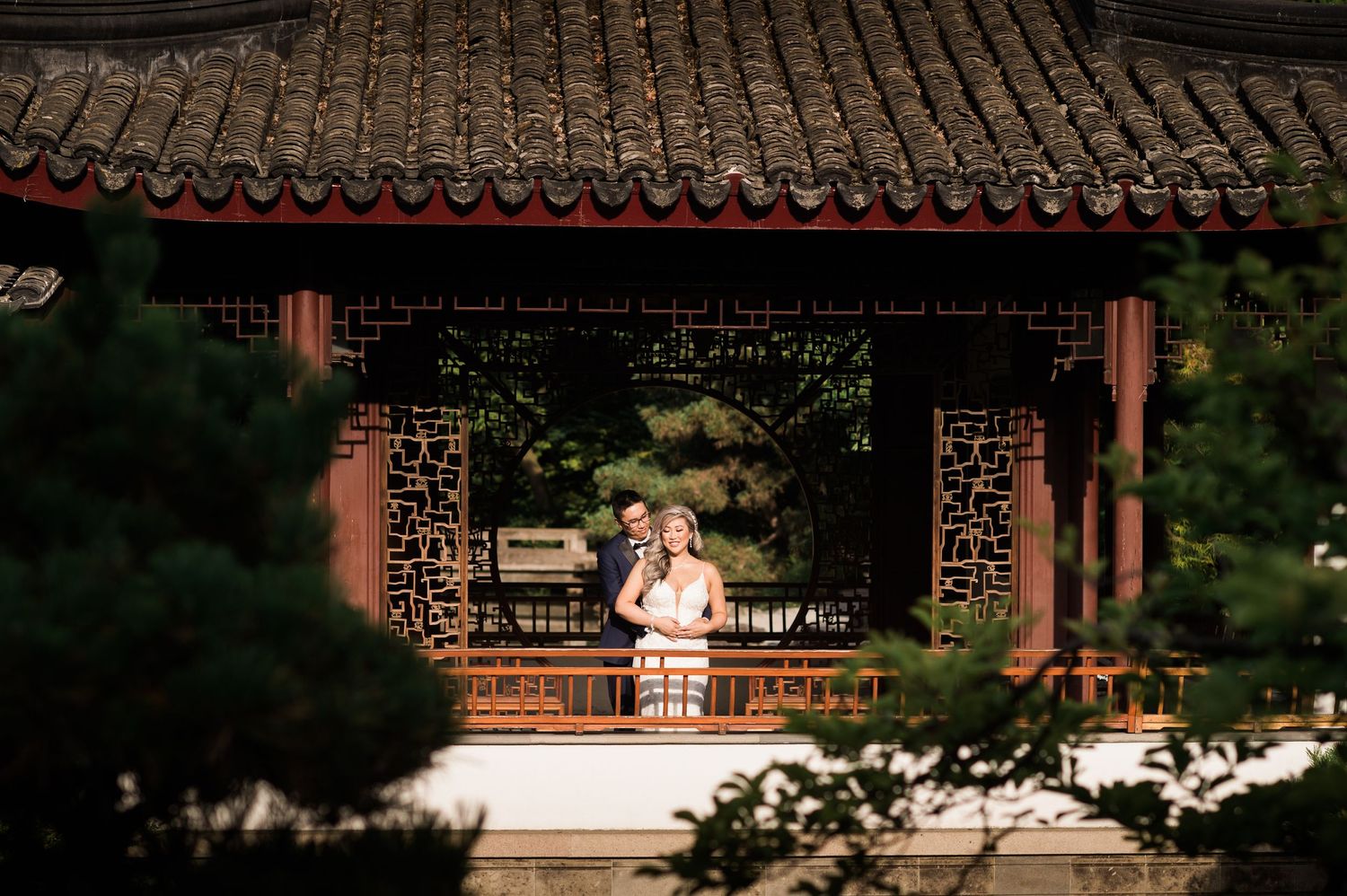 A couple sits together in a traditional Asian pavilion with ornate tiled roof and decorative details.