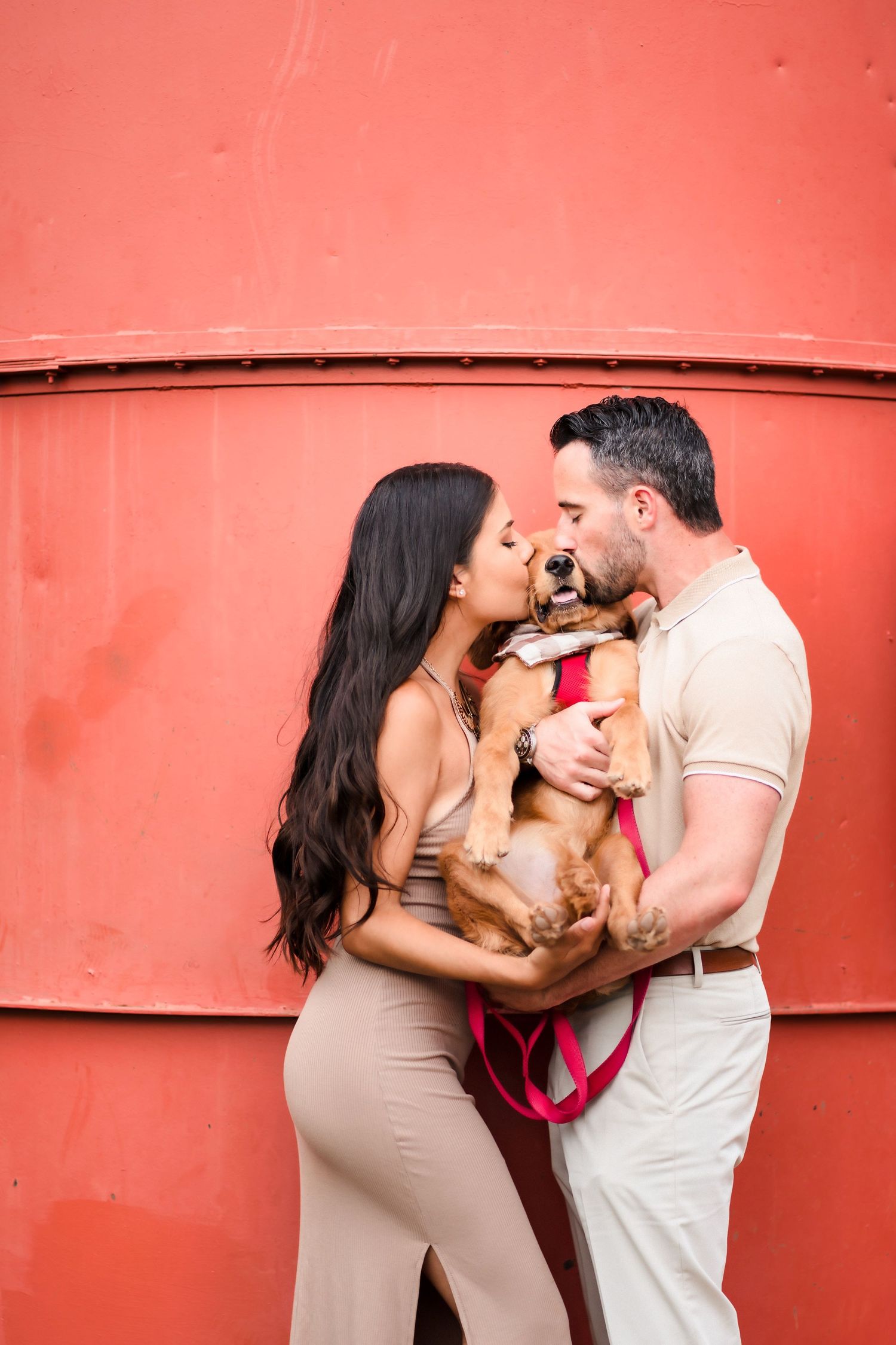 Couple sharing intimate moment with their dog against vibrant red wall background.