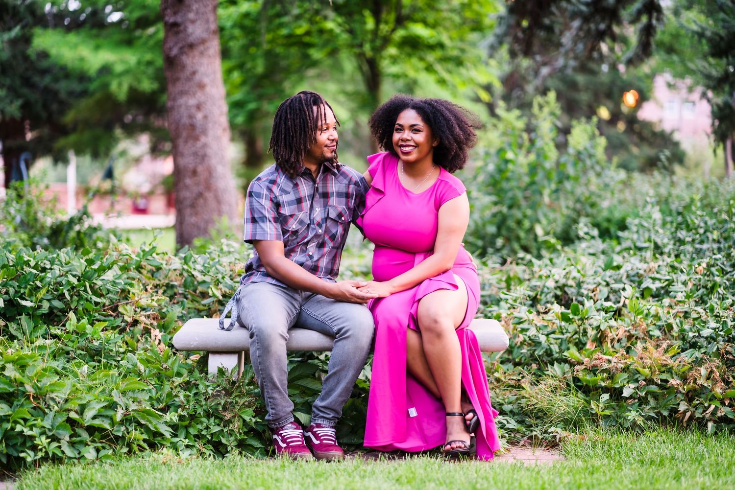 A couple laughs together while sitting on a bench in a lush garden setting.
