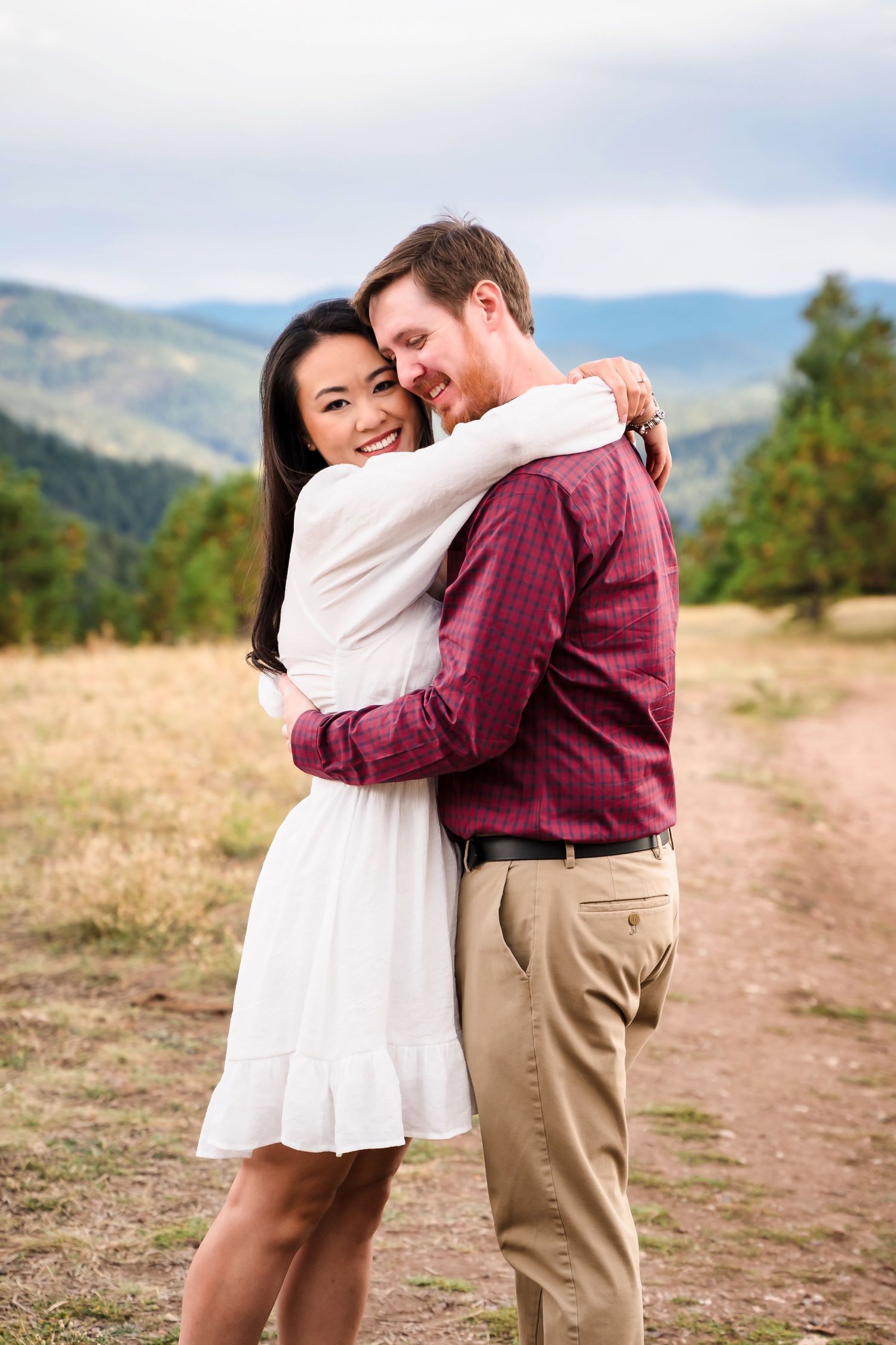 Couple embracing on a mountain trail with rolling hills in the background.