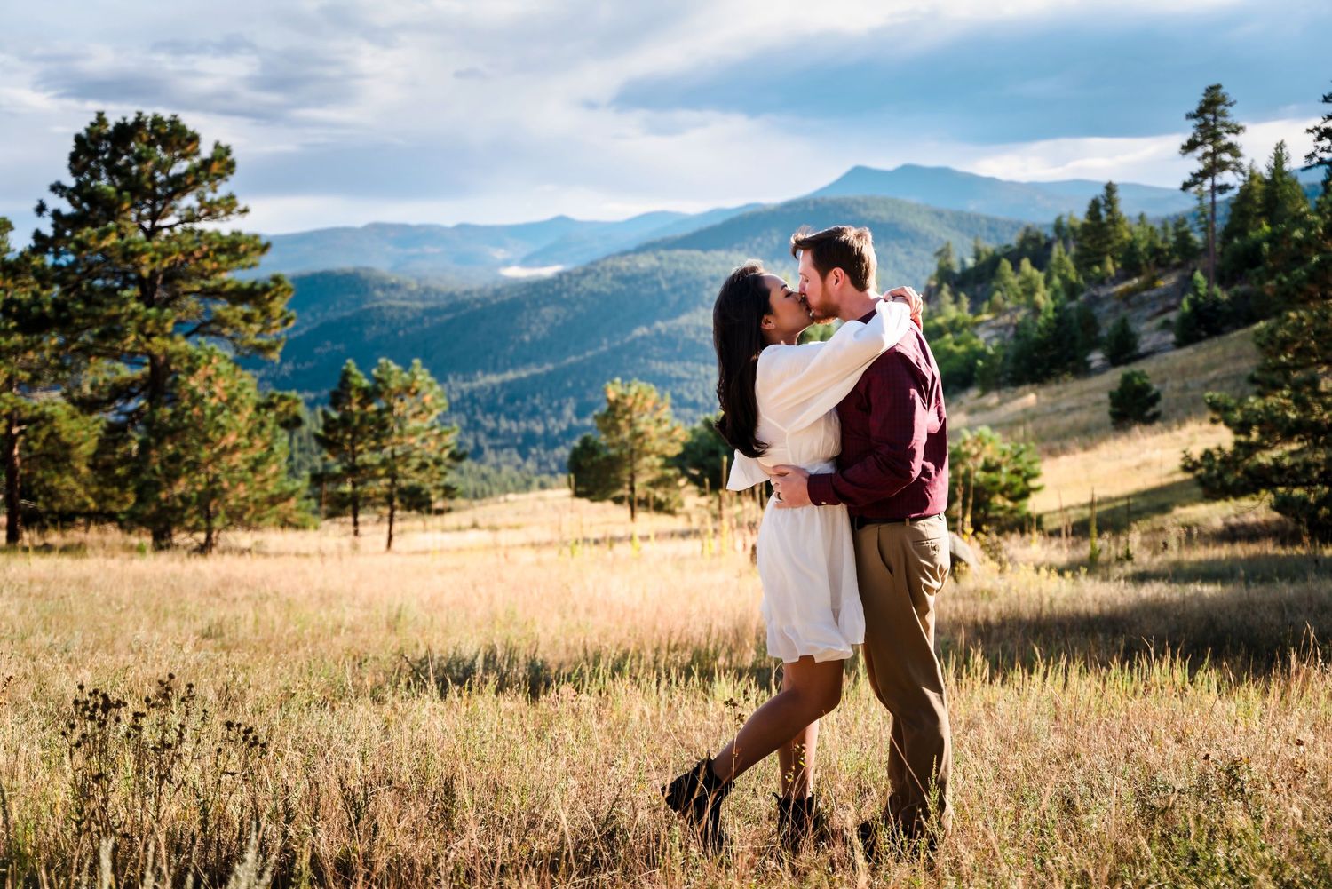 Couple embracing in a mountain meadow with dramatic landscape views.