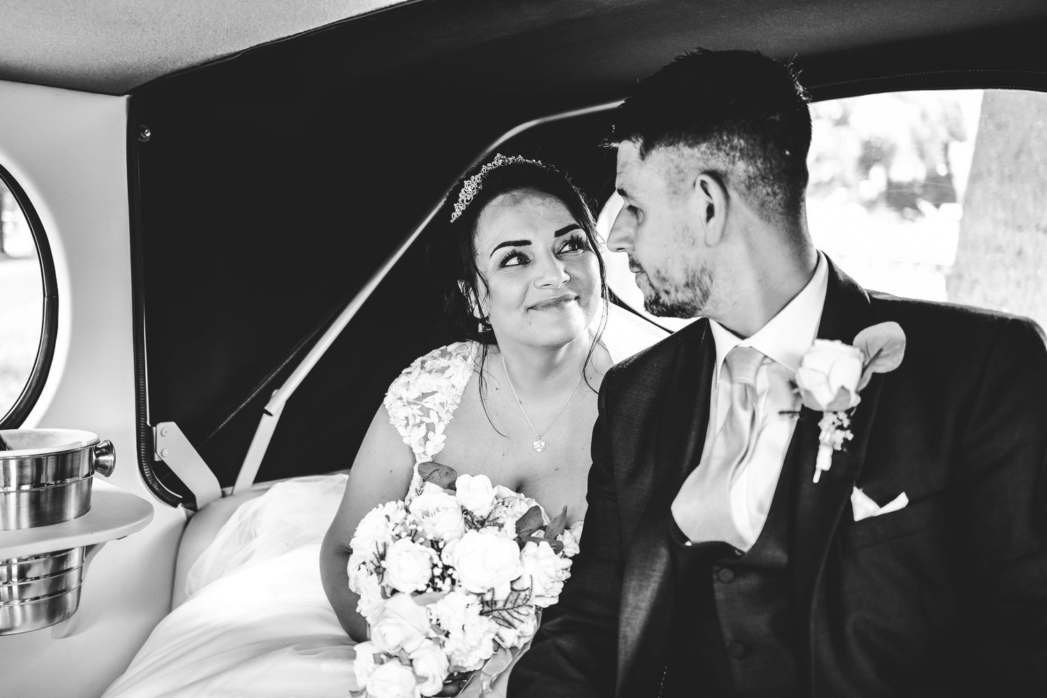 Bride devotedly staring into groom's eyes in their wedding car before heading off to their wedding venue.