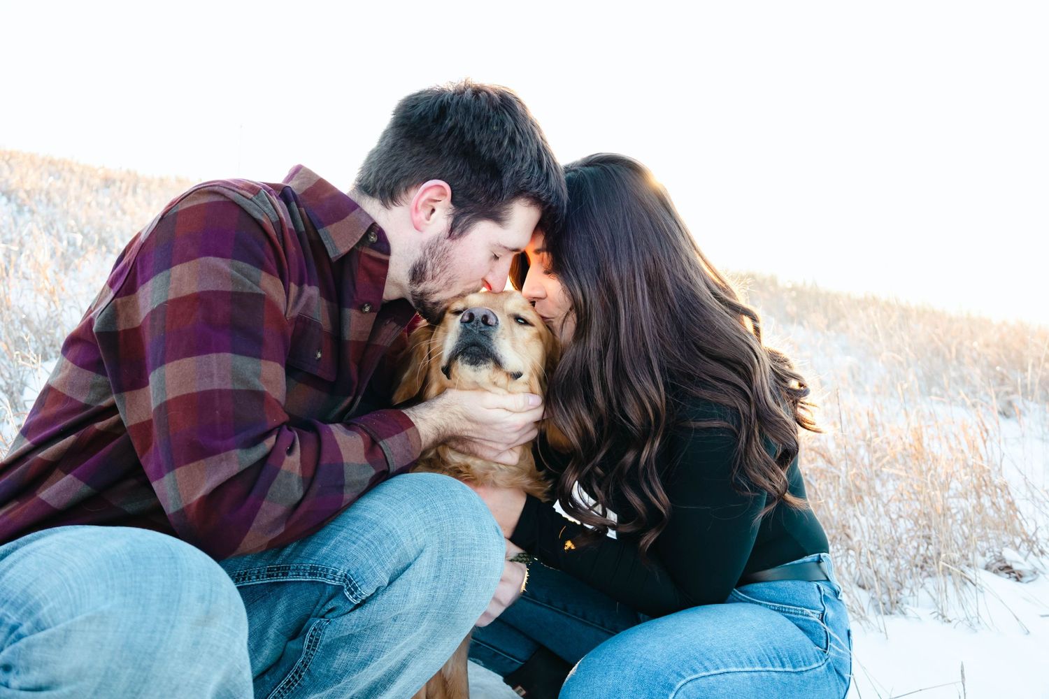 Couple sharing an intimate moment with their dog in a snowy winter setting.