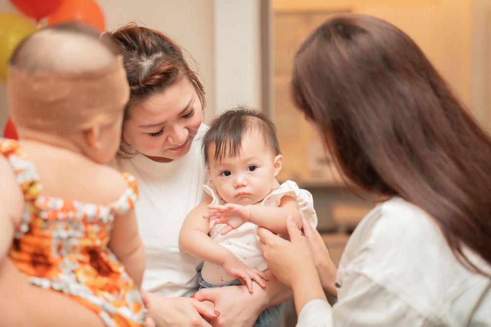 A group of people gathered around a baby in a room with orange balloons.