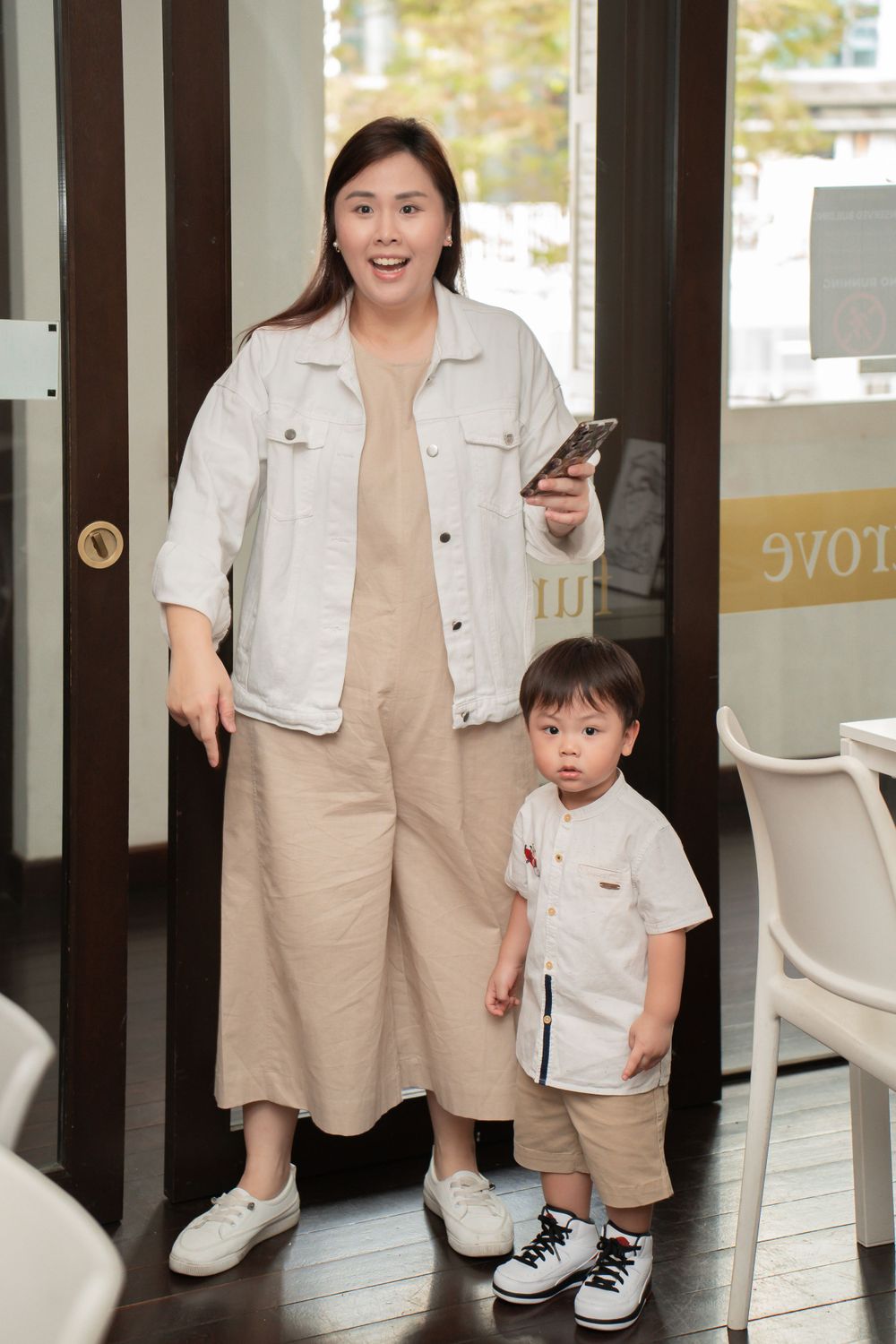 A matching casual beige outfit duo standing in a bright doorway.