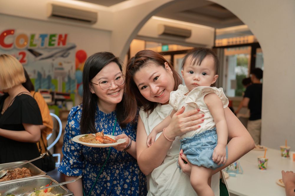 Group enjoys a celebratory moment with food and a small child at a decorated indoor venue.