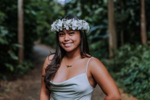 Person in gray dress and floral crown poses on forest path.