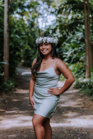 Person in silver dress and floral crown poses on wooded path.