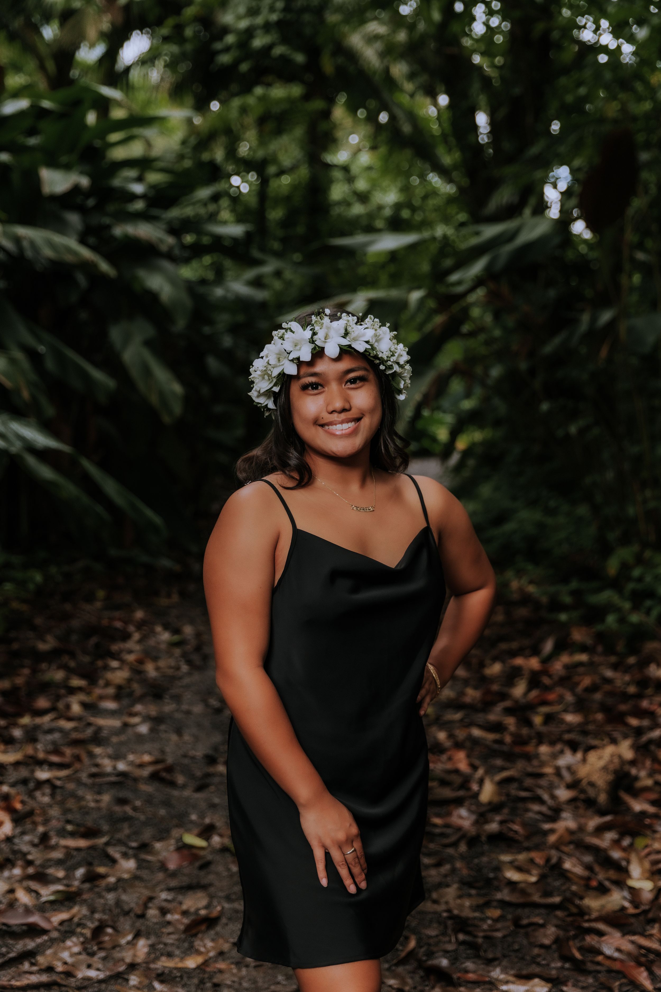 A person in a black top poses outdoors wearing a white floral crown.
