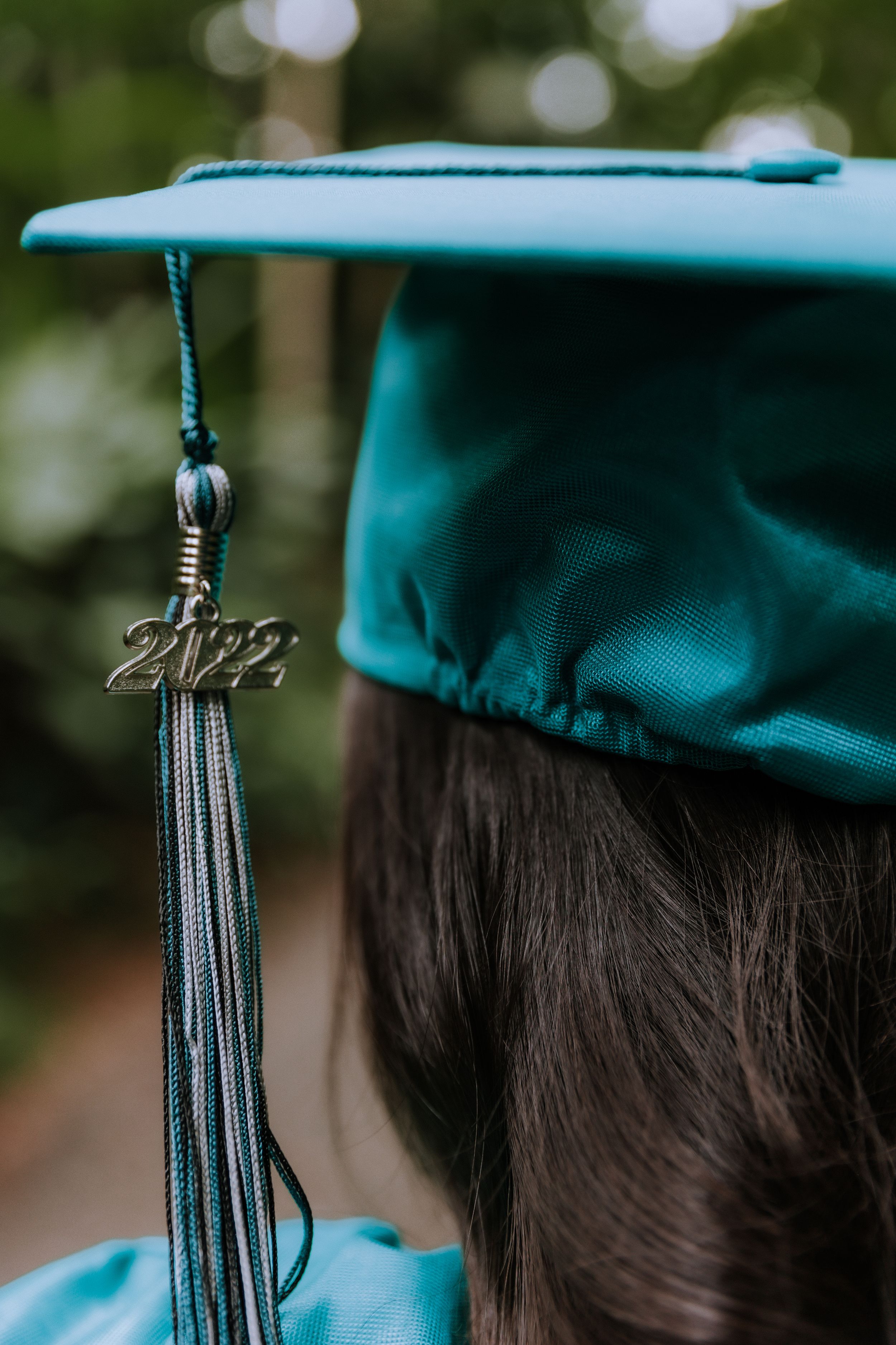 Close-up of teal graduation cap tassel against blurred background.