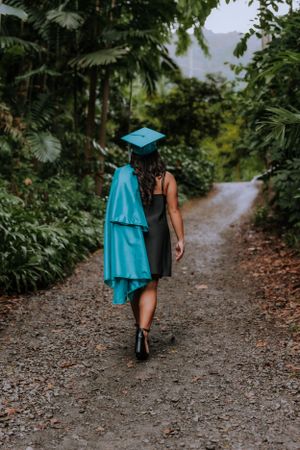 Person walking away on forest path wearing teal graduation gown.