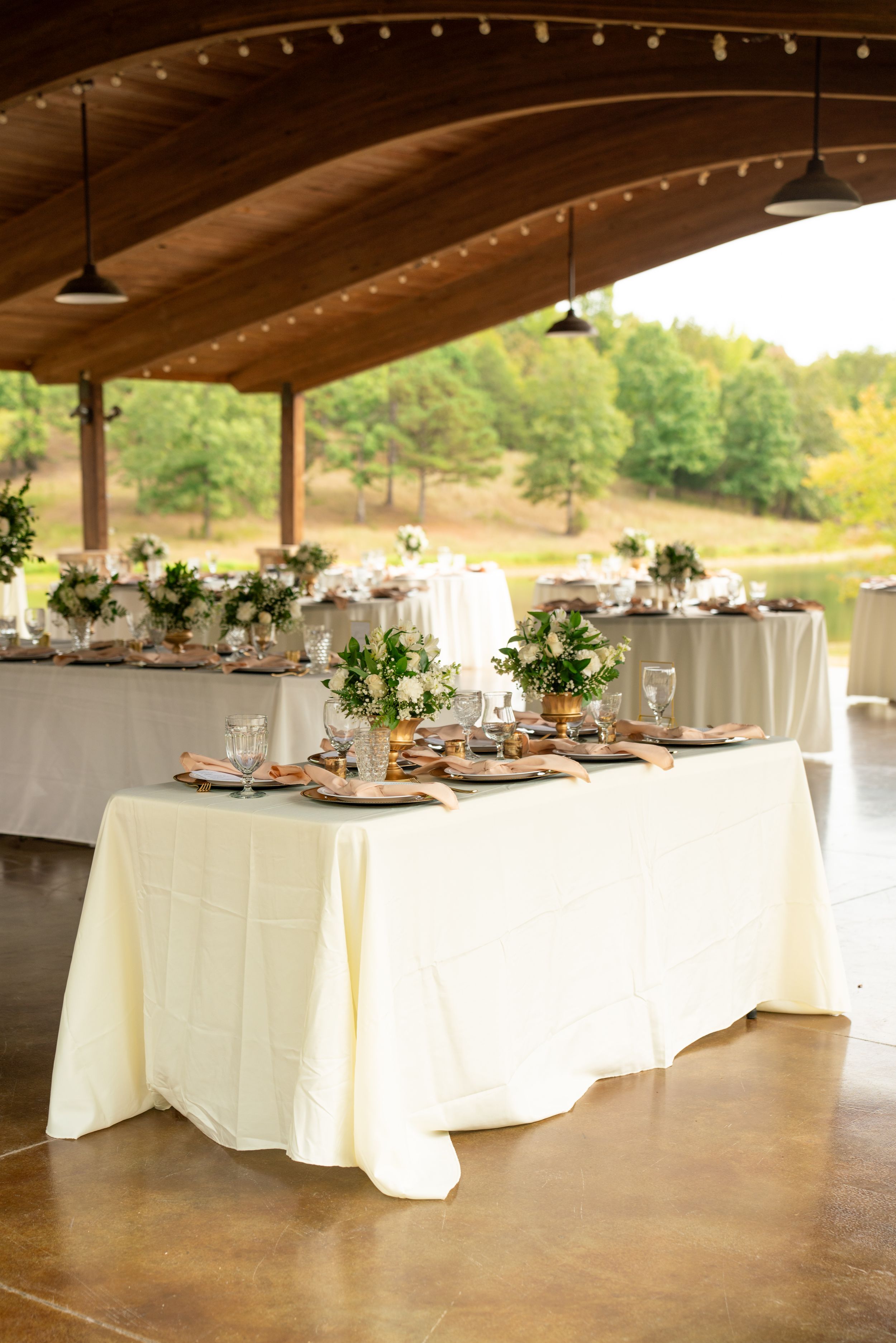 Elegant wedding reception setup with white tablecloths and string lights under wooden beams.