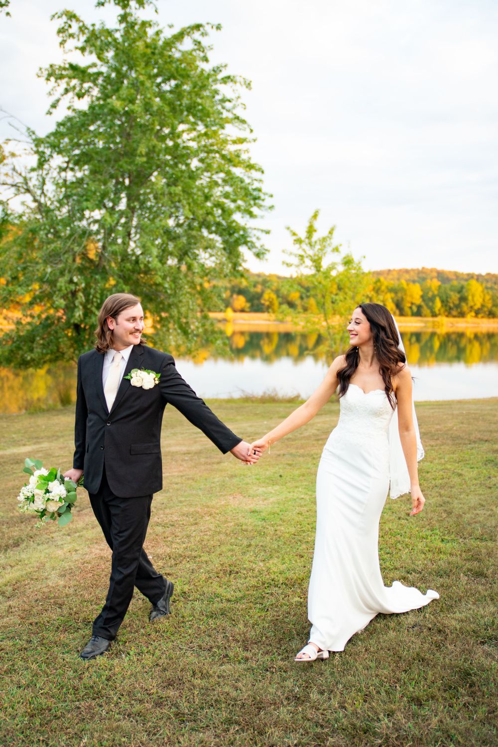 Wedding couple dances playfully in an open field with autumn colors in background.