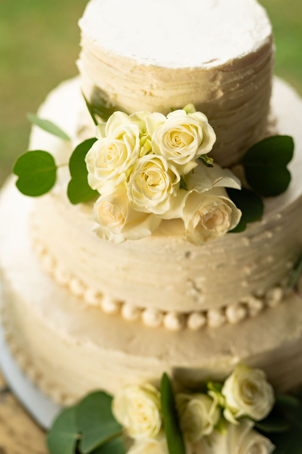 White wedding cake decorated with cream frosting and pale yellow roses.