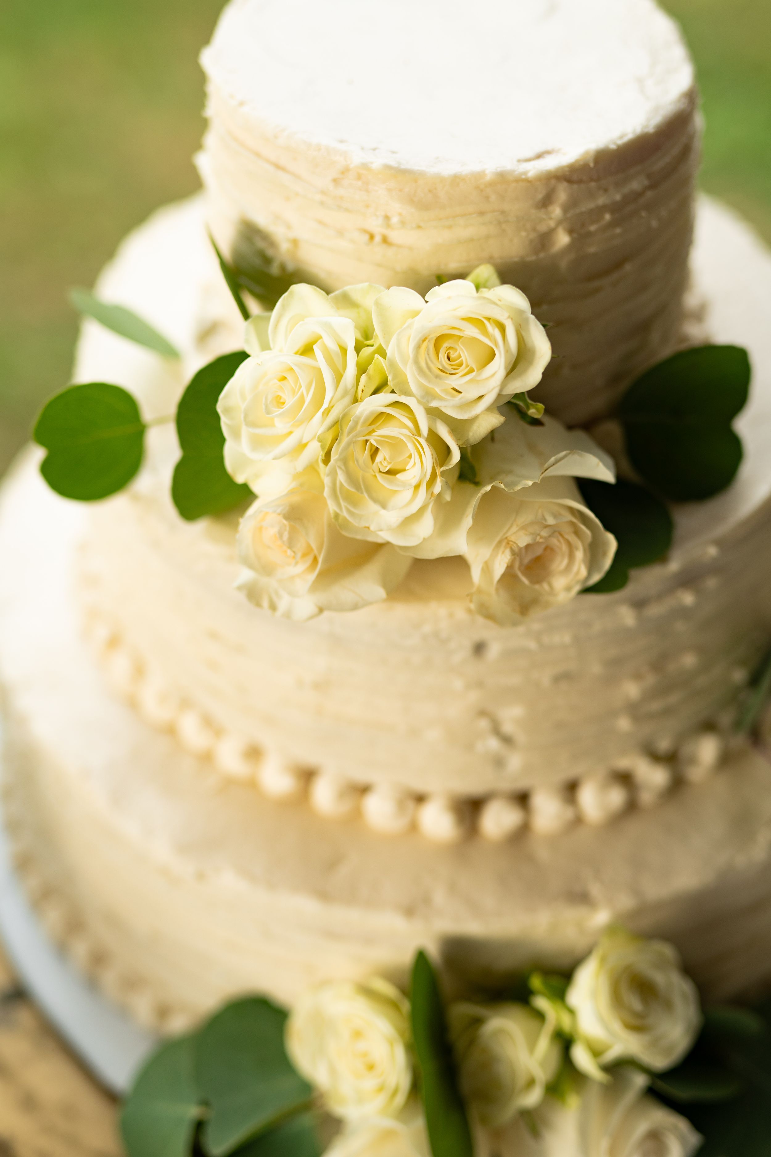 White wedding cake decorated with cream frosting and pale yellow roses.