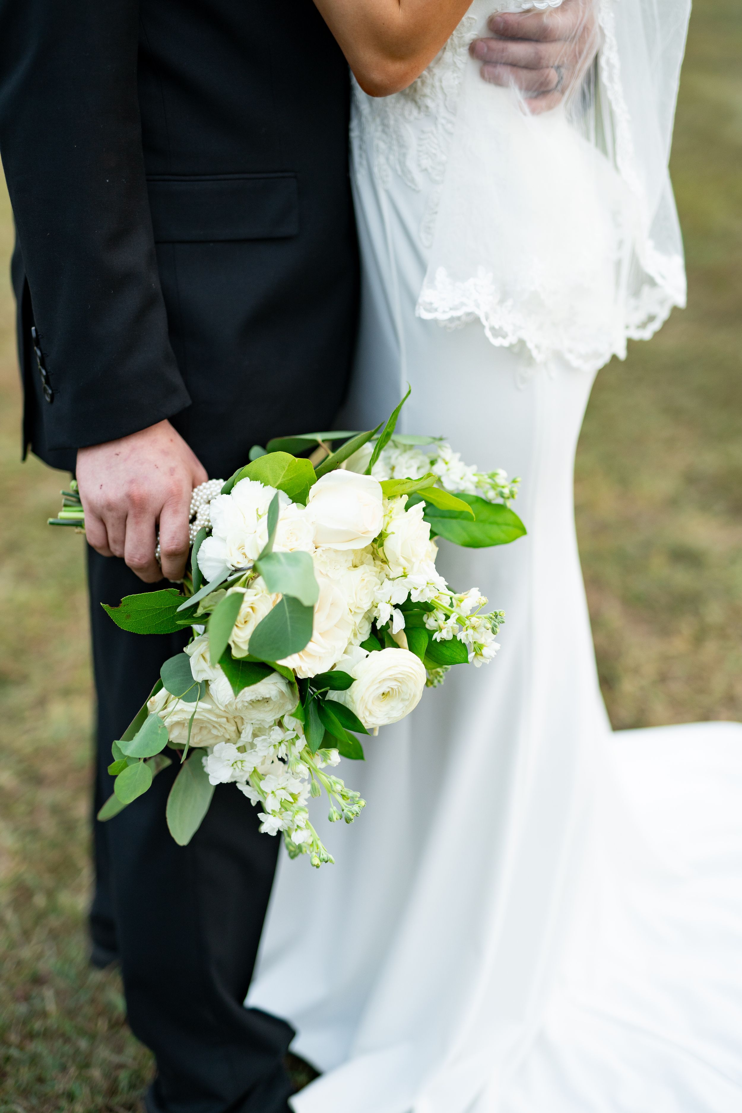 White wedding dress and black tuxedo shown with elegant white floral bouquet.