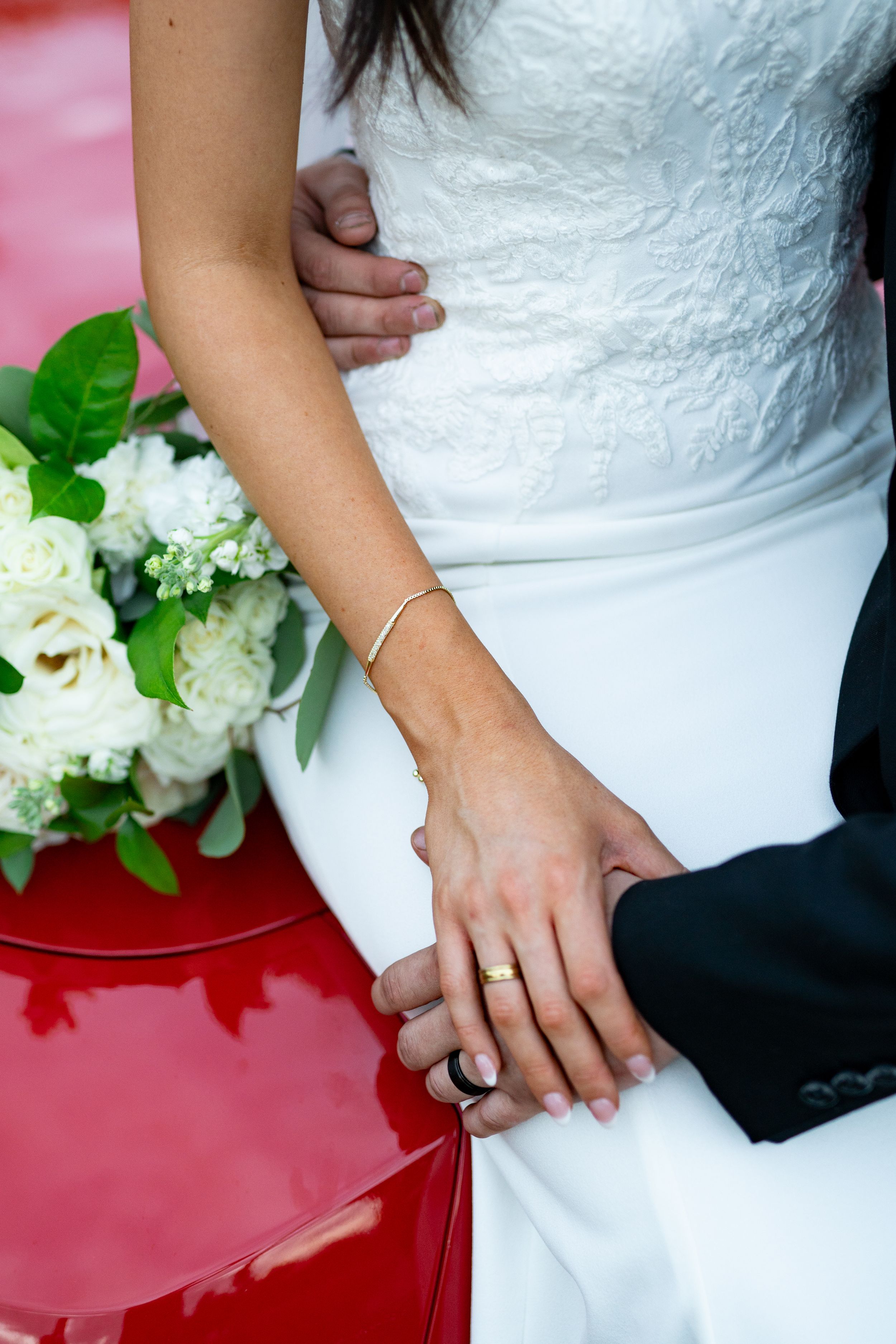 Close-up details of a bride's white lace dress and hands.