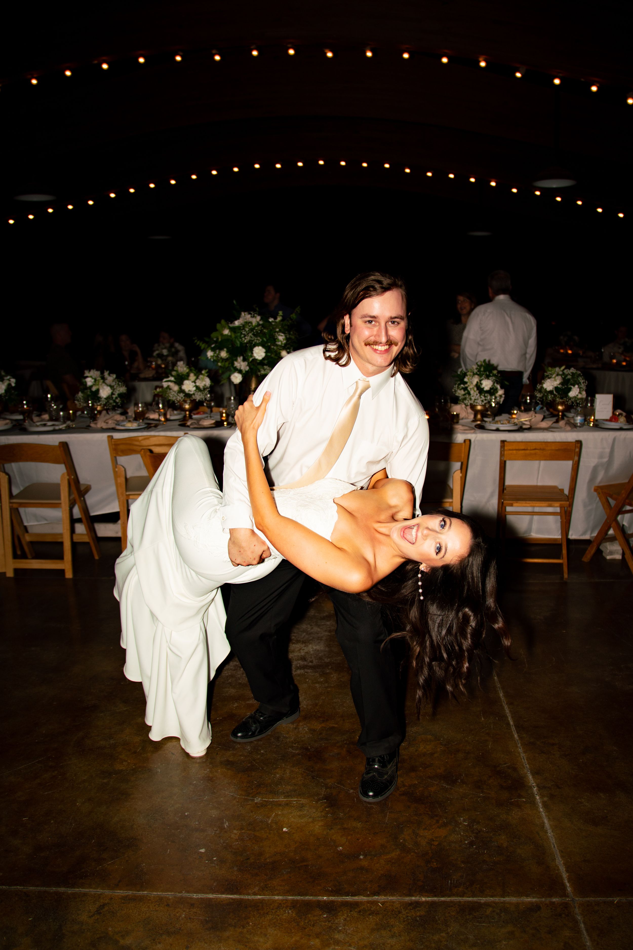 Dramatic dip dance move performed on an illuminated dance floor at a wedding reception.