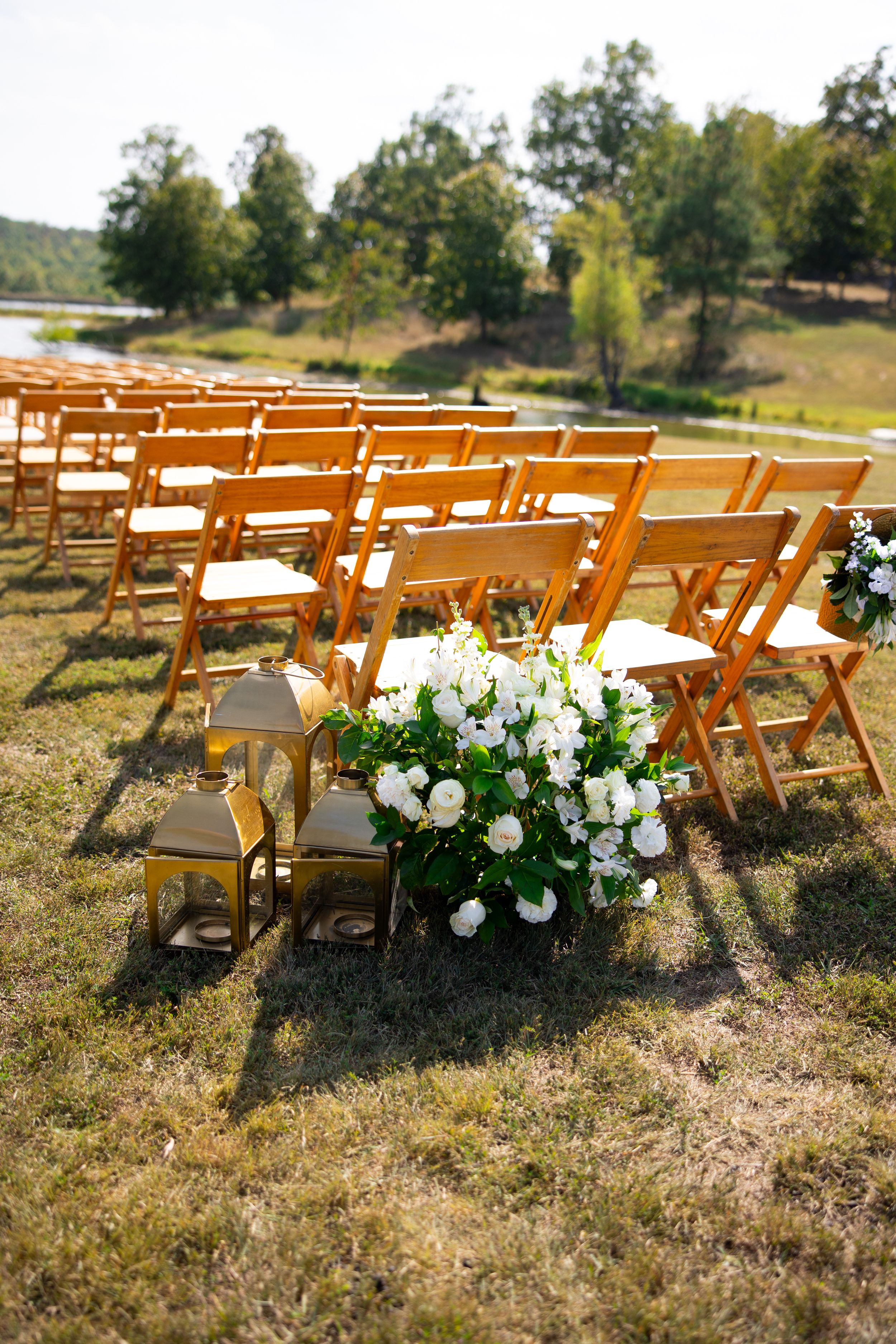 Wooden chairs set up for outdoor wedding ceremony with white floral decorations and lanterns.