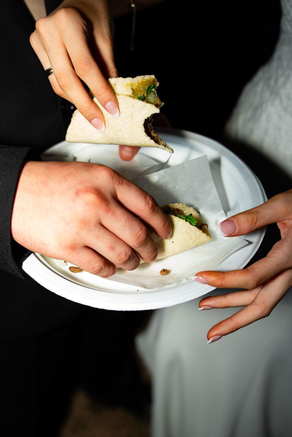 Close-up shots of hands holding white plates with food at a wedding reception.