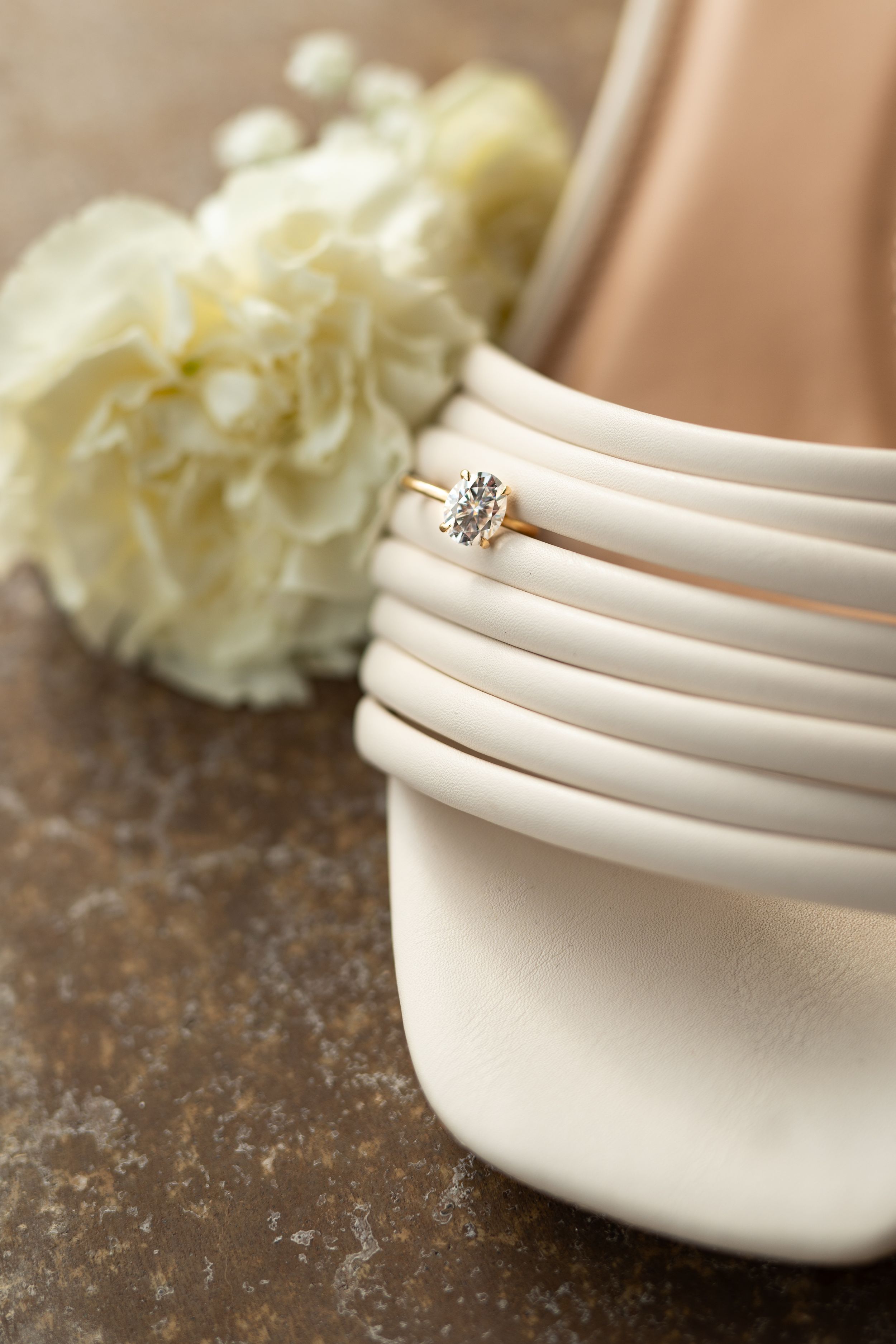 Close-up detail of white bridal shoes with wedding rings on textured background.