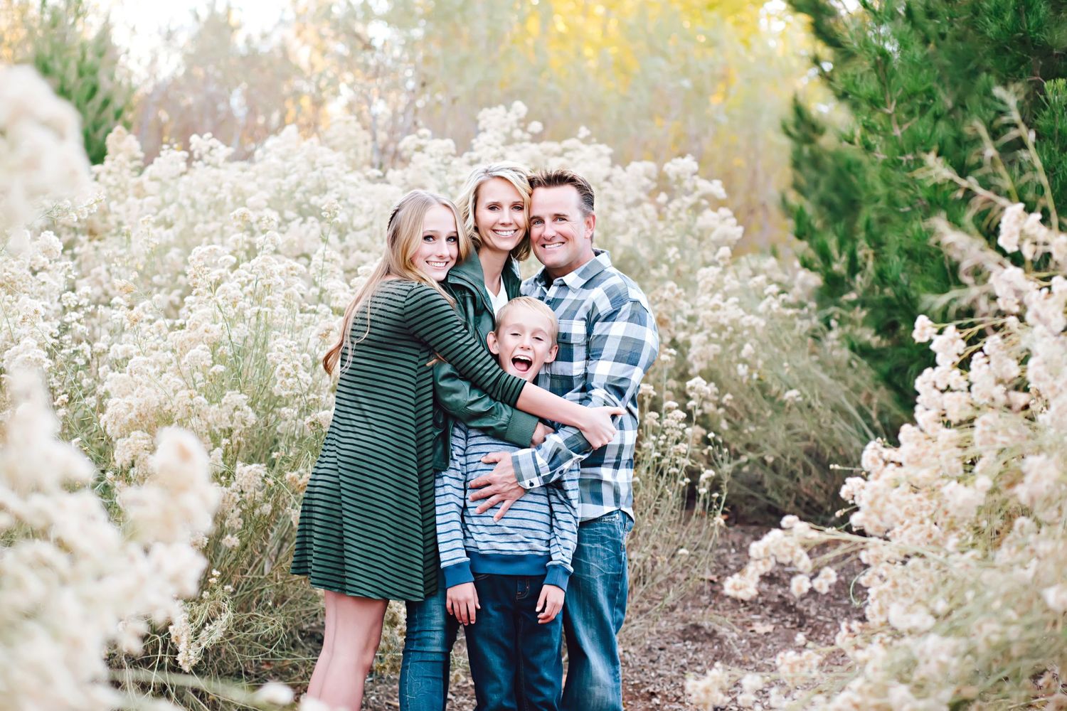 Happy family posing together outdoors among white wildflowers and autumn foliage.