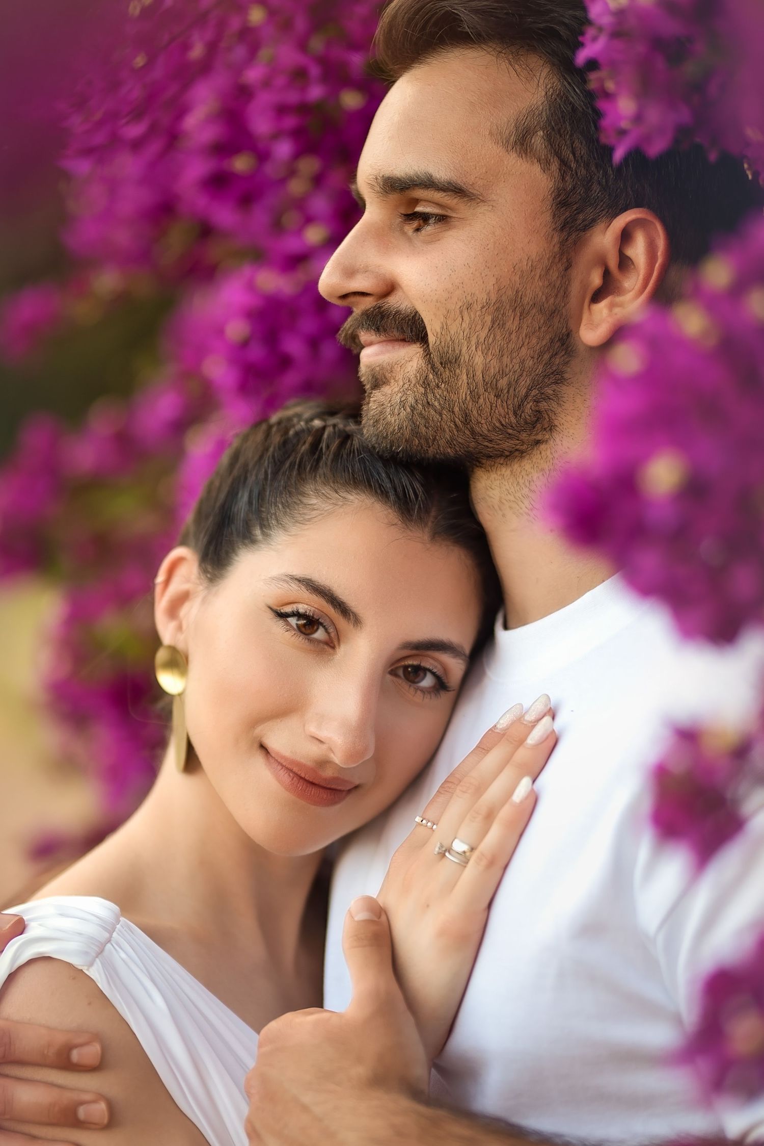 Engaged couple poses against vibrant purple bougainvillea flowers in intimate portrait.