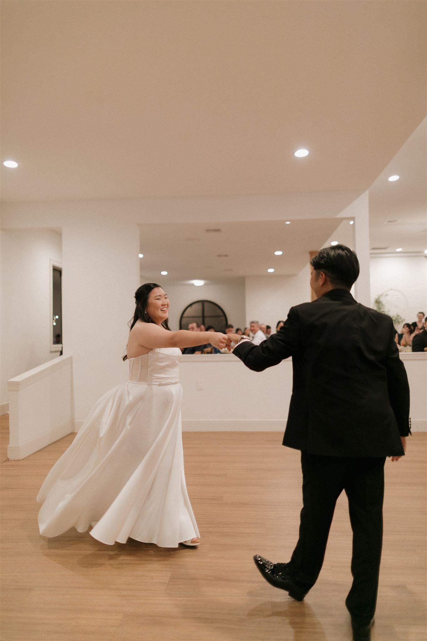 Wedding dance in modern venue with hardwood floors and white walls.