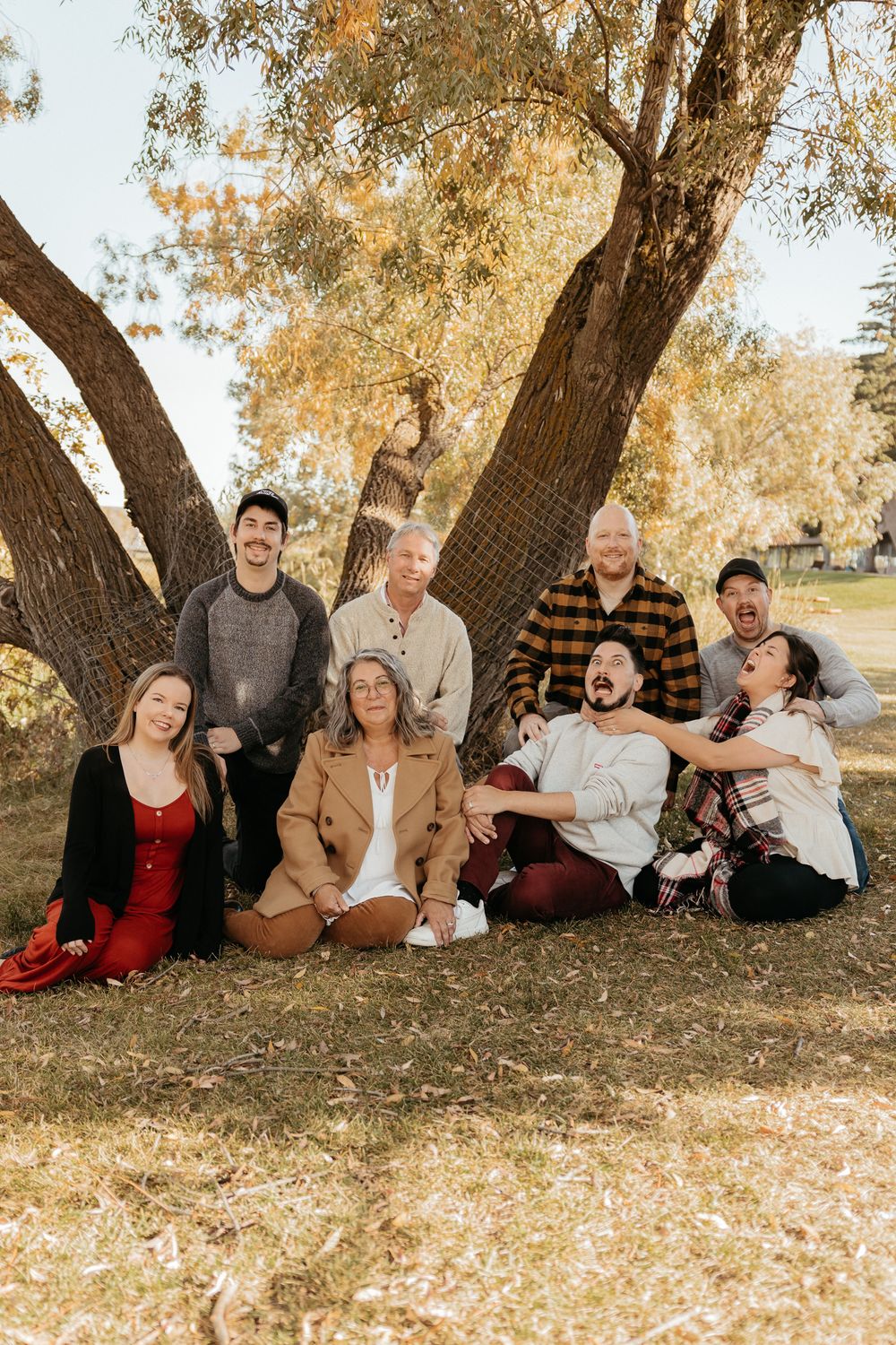Group portrait of people relaxing beneath a large tree with golden fall foliage.