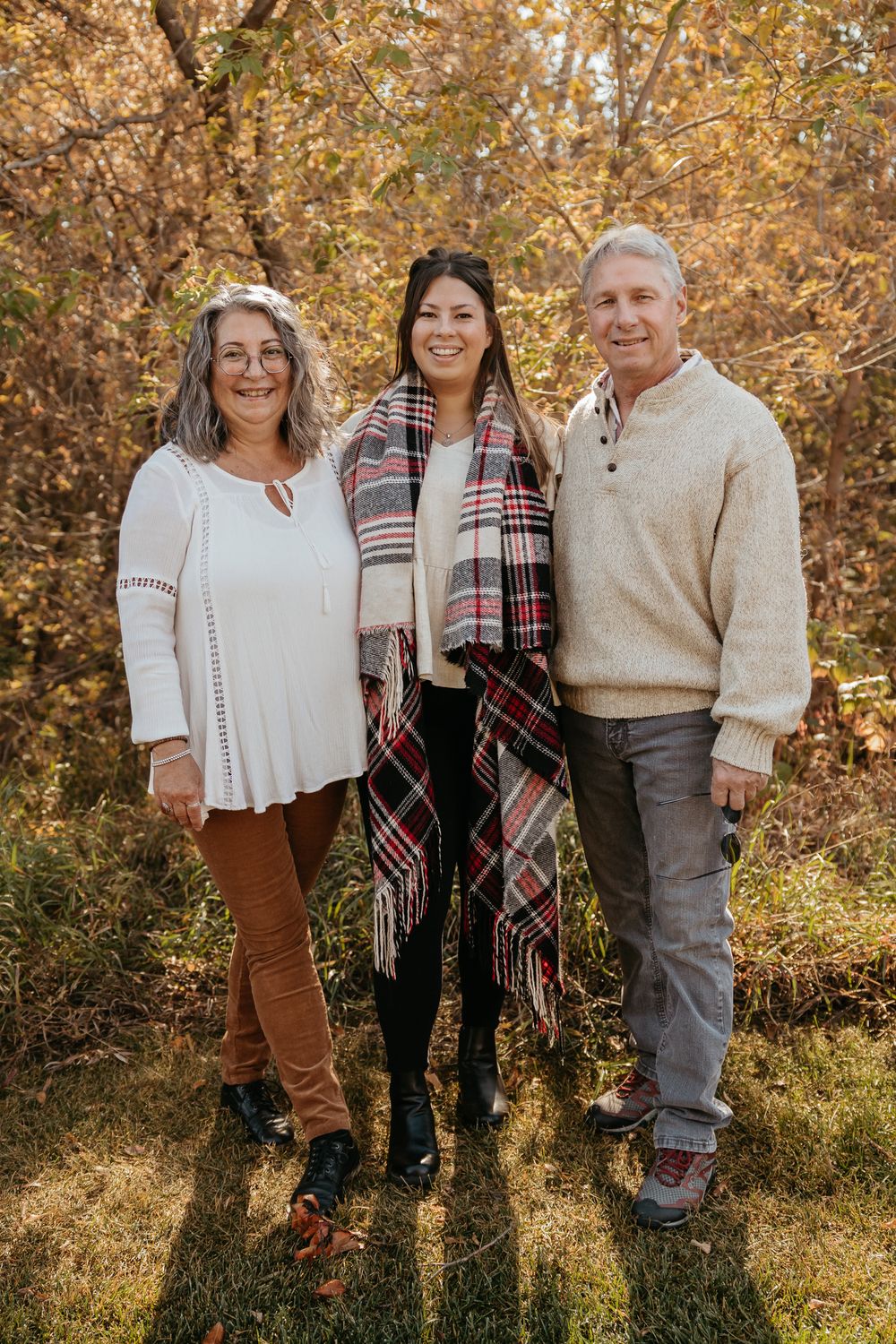 Small group portrait with coordinated outfits featuring plaid and cream colors in autumn setting.