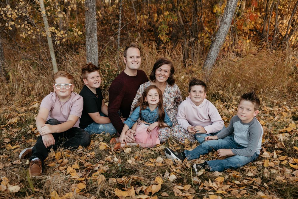 Family members pose together among fallen autumn leaves in a wooded setting.