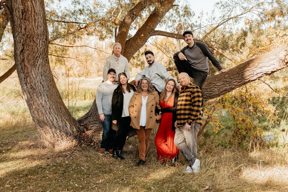 Family members gather beneath golden trees for outdoor portraits in warm autumn lighting.