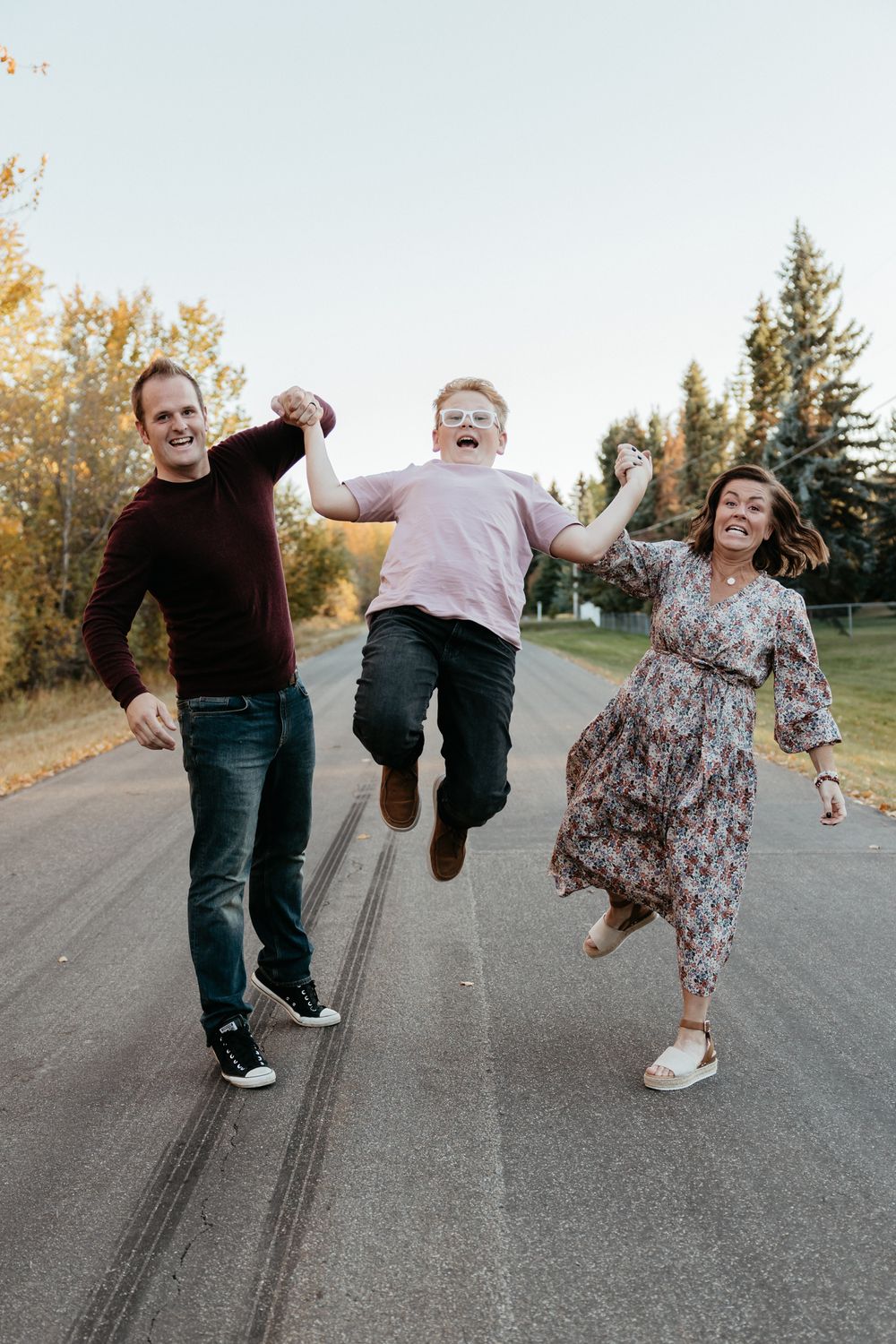 A joyful family moment captured mid-jump on a tree-lined road during autumn.